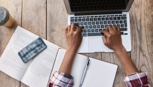 Person learning English online using laptop, notebook, and study materials at home